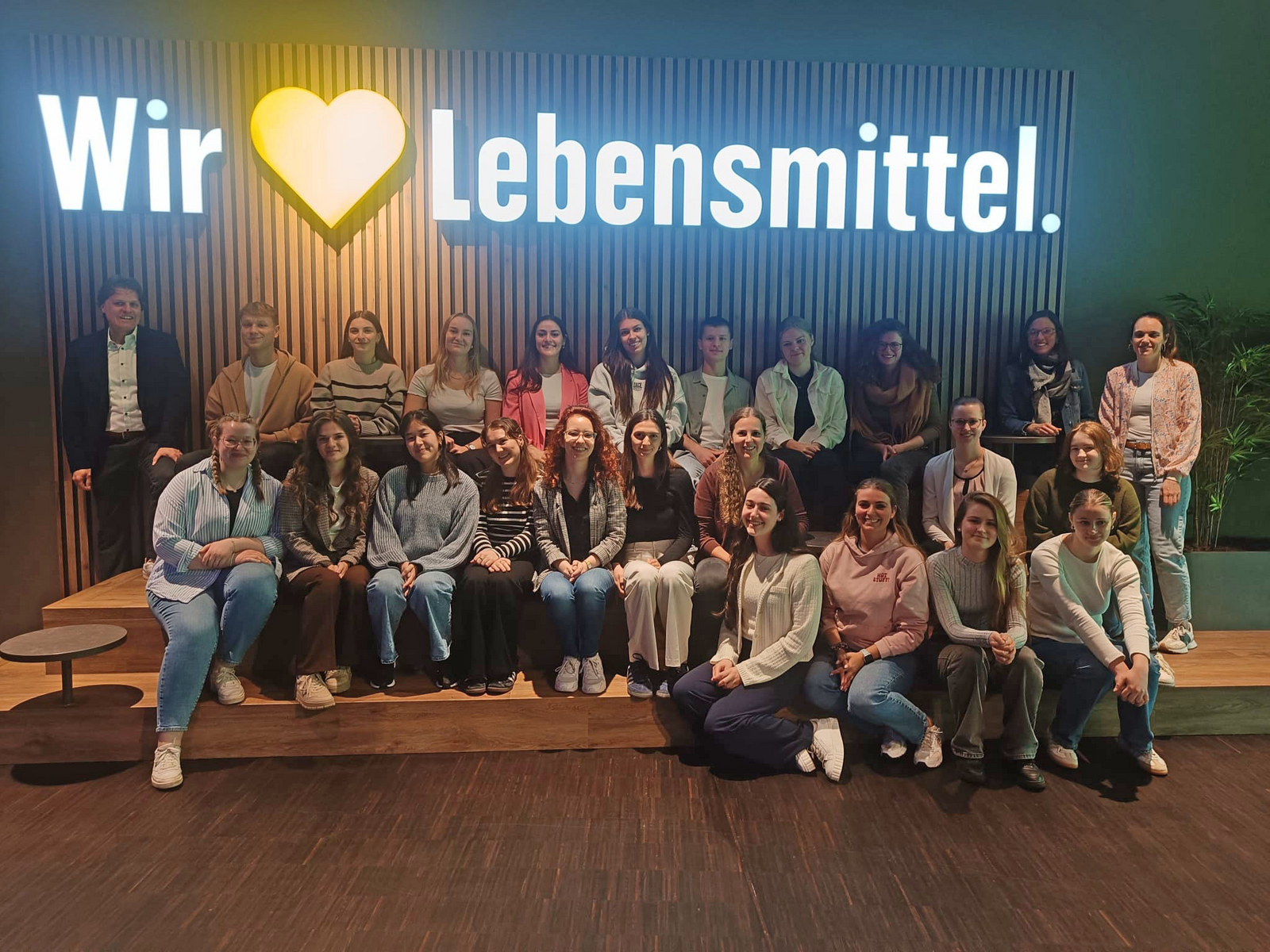 Gruppenfot von WP6-Studierende unter dem leuchtenden Edeka-Schriftzug "Wir lieben Lebensmittel"